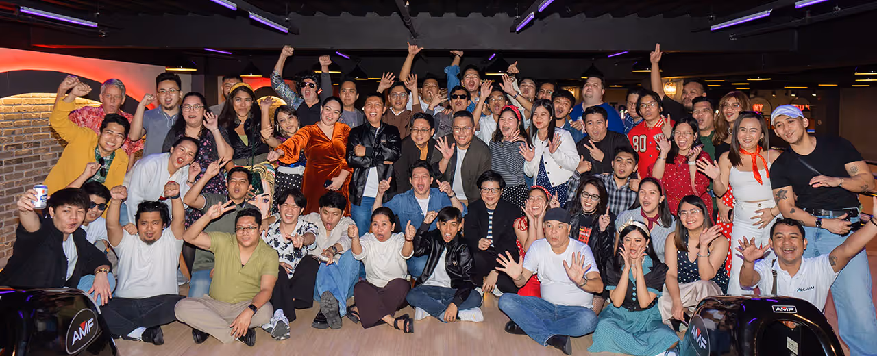 Large group of people posing joyfully at a bowling alley with raised hands and smiles.