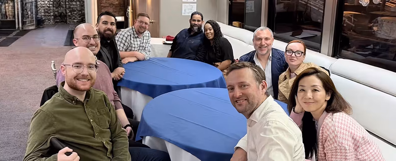 Group of ten people gathered around blue-linened cocktail tables, smiling at the camera.